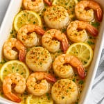 Oven-baked shrimp and scallops in a white baking dish with lemon slices, golden breadcrumb topping, and fresh parsley garnish.