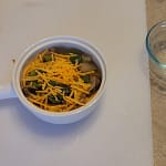A warm keto breakfast bowl filled with browned sausage, fluffy scrambled eggs, sautéed onions and peppers, and melted cheese, arranged in a rustic ceramic bowl on a wooden surface.