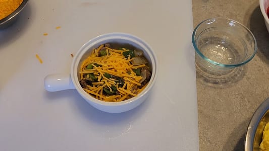 A warm keto breakfast bowl filled with browned sausage, fluffy scrambled eggs, sautéed onions and peppers, and melted cheese, arranged in a rustic ceramic bowl on a wooden surface.